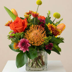 Mixed bouquet in a square glass vase with orange, pink, and yellow blooms