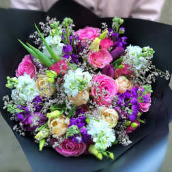 Hand-tied bouquet of pink, purple, white, and peach flowers wrapped in black paper