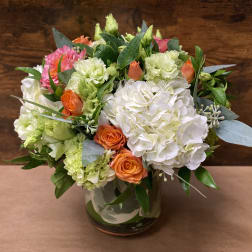 Mixed bouquet of white, pink, orange, and green flowers in a glass vase