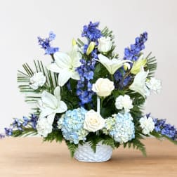White lilies, roses, hydrangeas, and blue flowers in a white basket