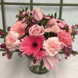 Pink mixed flower bouquet in a clear glass vase with a ribbon