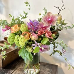 Mixed bouquet with orchids, roses, and green blooms in a glass vase