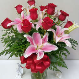 Bouquet of red roses and pink lilies in a glass vase with a red ribbon