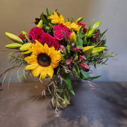 Bright mixed bouquet with sunflowers, pink roses, lilies, and a gold vase