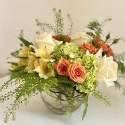 Mixed bouquet of roses, hydrangeas, and pale yellow flowers in a glass bowl vase