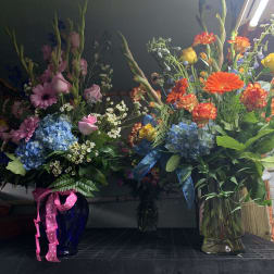 Two tall mixed flower arrangements in glass vases with ribbons
