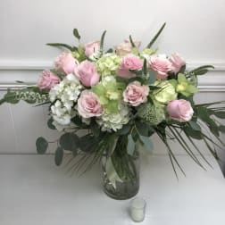 Large arrangement of pink roses, green orchids, and white hydrangeas in a clear glass vase with a small votive candle.