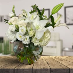 White lilies and roses arranged in a round glass vase