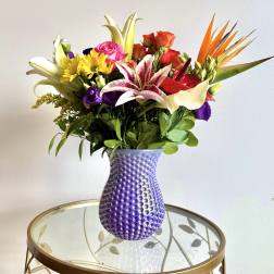 Mixed bouquet in a purple textured vase with lilies, roses, and daisies