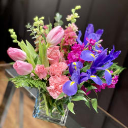 Pink tulips, roses, carnations, and purple irises in a glass vase