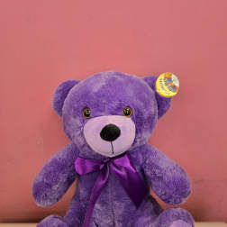 Purple teddy bear with a satin bow against a pink background