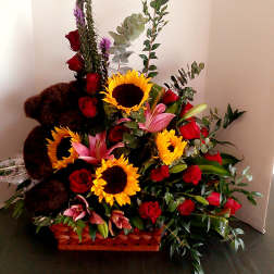 Basket arrangement with sunflowers, red roses, pink lilies, and a teddy bear