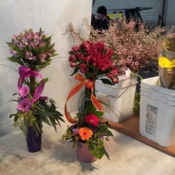 Three floral arrangements in buckets, including pink and red bouquets with ribbons