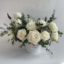 White roses arranged in a white vase with eucalyptus greenery