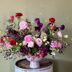 Mixed pink, red, and purple flowers in a white pedestal vase