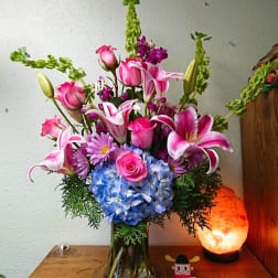 Pink lilies and roses with blue hydrangea in a glass vase