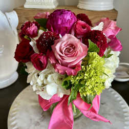 Pink and red mixed flower bouquet in a glass vase with a ribbon
