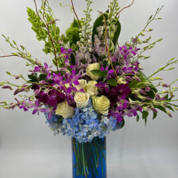 Tall mixed bouquet of orchids, roses, and blue hydrangeas in a blue vase