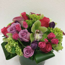 Pink and lavender roses with green orchids in a round vase