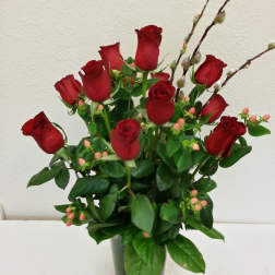 Red roses arranged in a clear glass vase with berry sprigs