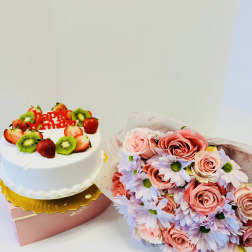 Birthday cake with fruit topping beside a pink rose and daisy bouquet