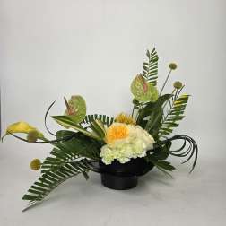Tropical floral arrangement in a black bowl with yellow and white blooms