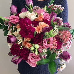 Large bouquet of pink, purple, and peach flowers held by a person