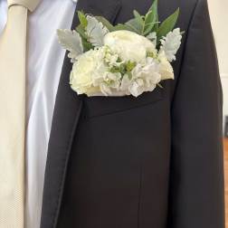 White boutonniere on a dark suit jacket with a cream tie