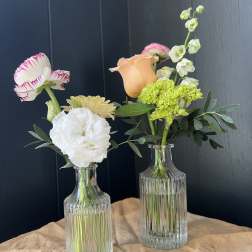 Two small floral arrangements in clear glass bottles with mixed blooms.