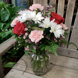 Mixed bouquet of red roses, white daisies, and pink carnations in a clear glass vase