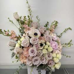 Large pastel floral arrangement in a white vase with roses and anemones