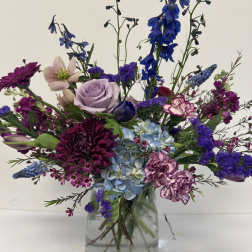 Mixed purple and blue flowers arranged in a clear glass vase