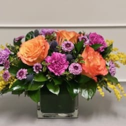 Orange roses and purple flowers in a square glass vase