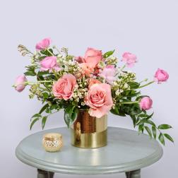 Pink roses and ranunculus in a gold vase with a small candle holder