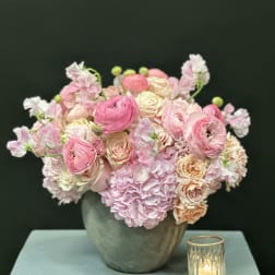 Pink and cream floral arrangement in a gray vase beside a small candle holder
