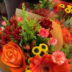 Bouquet of orange and red flowers with yellow accents wrapped in paper