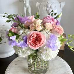 Pastel bouquet of roses, hydrangeas, and purple blooms in a glass vase