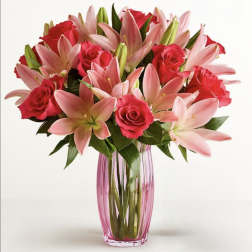 Pink lilies and red roses arranged in a tall glass vase