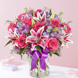 Pink roses and lilies in a glass vase with a purple ribbon