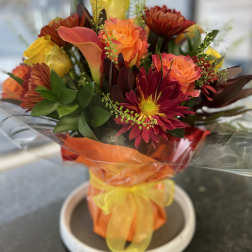 Bouquet of orange and red flowers wrapped in orange cellophane with a yellow ribbon