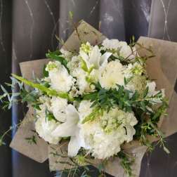 Hand-tied bouquet of white lilies and hydrangeas wrapped in brown kraft paper