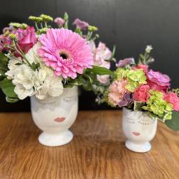 Two floral arrangements in white face vases on a wooden table