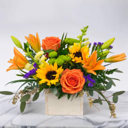 Orange roses and sunflowers in a wooden box with purple accents