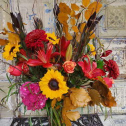 Autumn bouquet with sunflowers, red lilies, and orange leaves in a glass vase