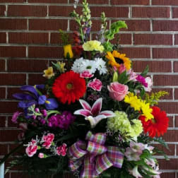 Colorful mixed flower arrangement in a glass vase with a plaid ribbon