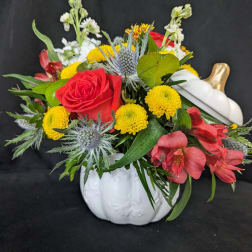 Mixed bouquet with red roses, yellow mums, and pink flowers in a white pumpkin vase