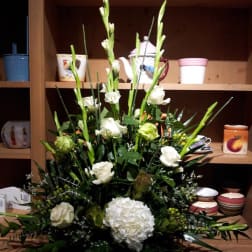 Tall white floral arrangement with roses, hydrangea, and gladiolus in a container