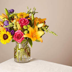 Mixed bouquet of roses, lilies, and sunflowers in a glass vase