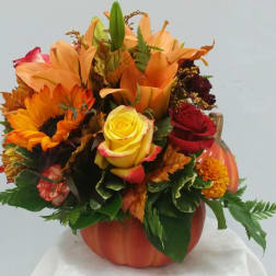 Autumn bouquet in a pumpkin-shaped vase with sunflowers, roses, and lilies