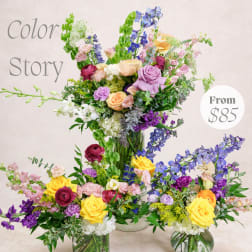 Colorful mixed flower arrangements with roses, delphinium, and orchids in glass vases